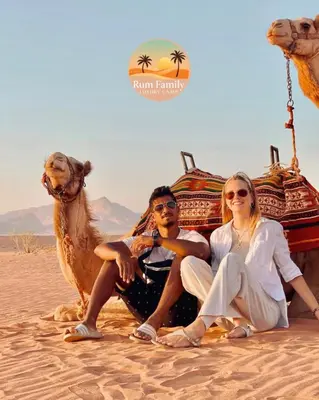 a man and woman sitting next to a camel in the desert at RUM fAMILY lUXURY CAMP in Wadi Rum