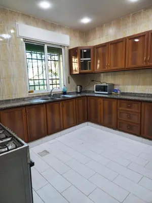 a kitchen with wooden cabinets and a white tile floor at Monani in Amman
