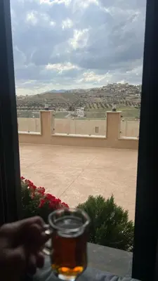 a person sitting at a table looking out a window at a patio at شاليهات إيليت بانوراما فيو in Jerash