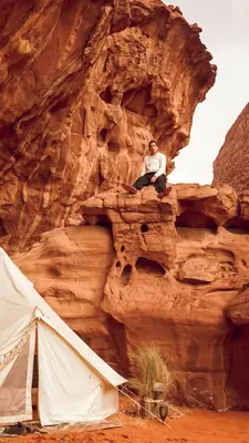 a man sitting on top of a cliff next to a tent at The Legacy of Wadi Rum in Wadi Rum