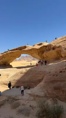 a group of people walking in the desert under a bridge at Rotana Wadi Rum in Wadi Rum