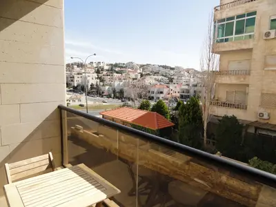 a balcony with two chairs and a view of a city at Dair Ghbar Apartment in Amman