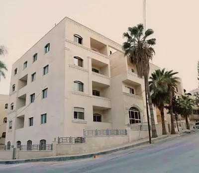 a white building with palm trees in front of it at EVANNA SUITE AND HOTELs ايفانا للشقق الفندقيه و المفروشه in Amman