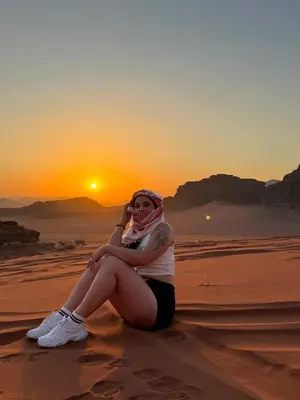 a woman sitting in the desert watching the sunset at cave under the stars in Wadi Rum