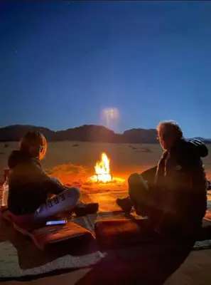 two people sitting around a fire in the desert at Wadi Rum Bubbles Luxury Camp in Wadi Rum