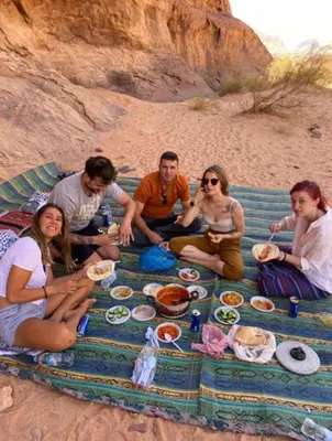 a group of people sitting around a picnic table on the beach at Wadi Rum Bubbles Luxury Camp in Wadi Rum