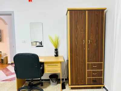 a desk with a chair next to a wooden cabinet at شقة واسعة وهادئة in Umm Juraysāt