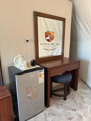 a room with a desk and a mirror next to a table with a refrigerator at Nova Rum Luxury Camp in Disah