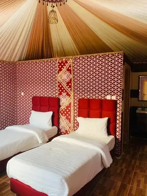 two beds in a room with a red wall at Sand Desert Camp in Wadi Rum