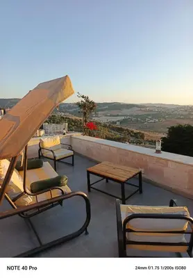 a patio with chairs and tables and an umbrella at panorama tal elroman chalet in Tal‘at ar Ruzz