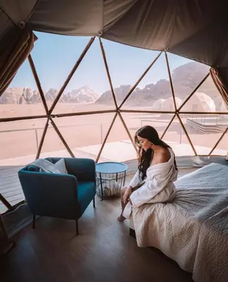 a woman sitting on a bed in a tent at RUM Bubble lUXURY CAMP in Disah