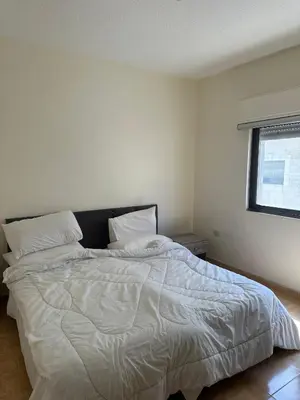 a bedroom with a large bed with white sheets and a window at الجبيهة 2 نوم aljubiha apartment in Amman