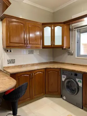a kitchen with wooden cabinets and a washing machine at Shmeisani Cozy Apartment in Amman