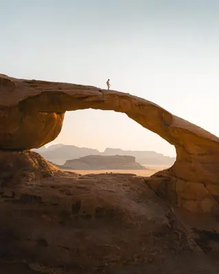 a person standing on top of an arch in the desert at Moon House & Sunset Tour in El Quweira