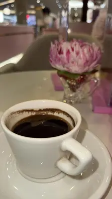 a cup of coffee sitting on a table with a vase of flowers at Furnished family apartment near the University of Jordan - Al-Jabihah in Amman