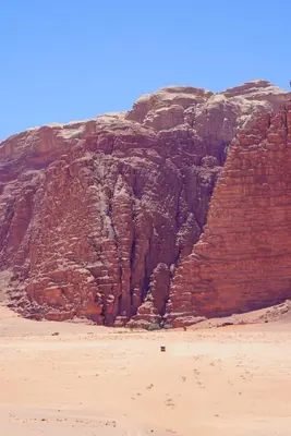a large rock cliff next to a sandy beach at Dune Camp Tours in Wadi Rum