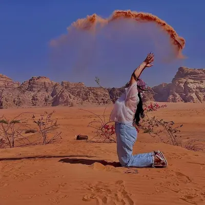 a woman in the desert with her hand in the air at Spirit of the Badia camp in Disah