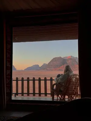 a woman sitting in a chair looking out a window at the desert at Wadi Rum Aura Camp in Wadi Rum