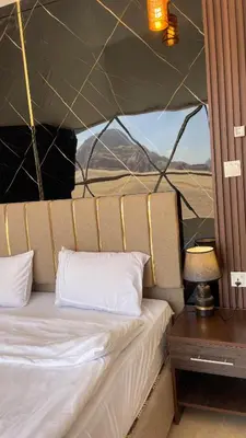 a bed in a tent with a table and a lamp at TALA lUXURY CAMP in Wadi Rum