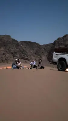 a group of people sitting in the sand near a car at Starlight Camp in Disah