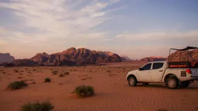 a white truck in the desert with mountains in the background at Wadi Rum Sands Story Camp &Tours in Wadi Rum