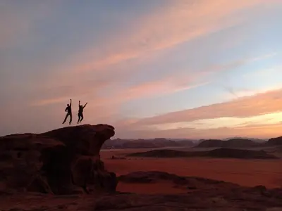 two people jumping off a rock in the desert at Wadi Rum Sands Story Camp &Tours in Wadi Rum