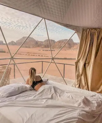 a woman laying in bed looking out at the desert at Wadi rum Hi camp in Wadi Rum