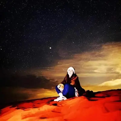 a woman sitting on the desert under a starry sky at Wadi rum tenda camp in Wadi Rum
