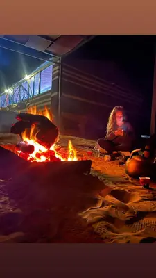 a woman sitting next to a fire in a oven at Noor Luxury Camp Wadi Rum in Wadi Rum