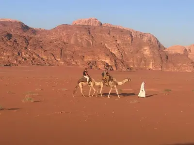 a group of people riding camels in the desert at Fire bedouin camp in Wadi Rum