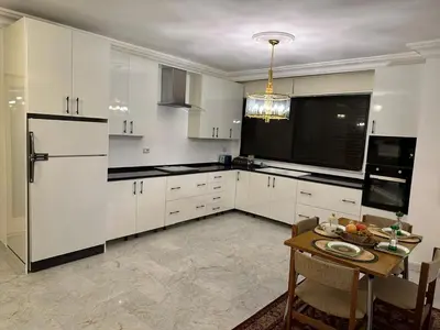 a white kitchen with a table and a refrigerator at Abdoun rose in Amman