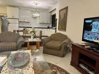 a living room with a tv and a table and a kitchen at Abdoun rose in Amman