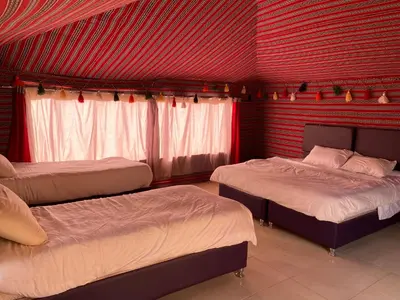 a room with three beds and a red wall at Rum Tale Camp in Wadi Rum