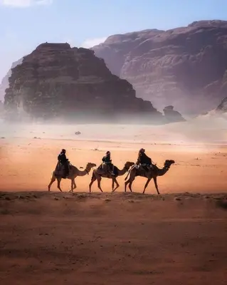 three people riding on camels in the desert at Silent Sands Lodge in Disah