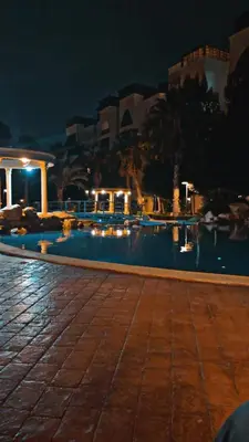 a large swimming pool at night with buildings in the background at Al qaoud apartment in Aydūn