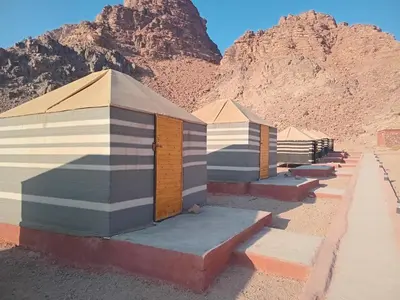 a row of beach huts with a mountain in the background at Ayed Wadi Rum camp in Wadi Rum