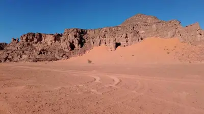 a desert with a mountain and a dirt road at faisal wadi rum in Wadi Rum