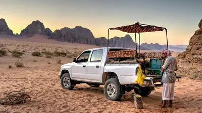 a man standing next to a white truck in the desert at Nomad Heights Authentic Bedouin Cave Experience in Wadi Rum in Wadi Rum