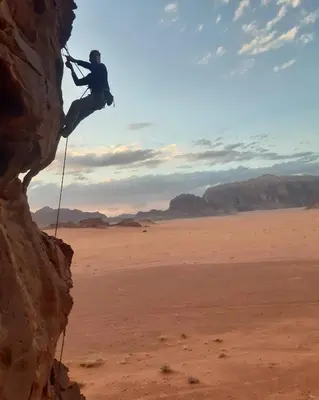 a man is climbing a rock in the desert at Rum Adventures Hostel in Wadi Rum