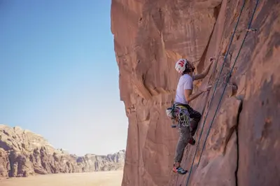 a woman is climbing a rock wall in the desert at Rum Adventures Hostel in Wadi Rum