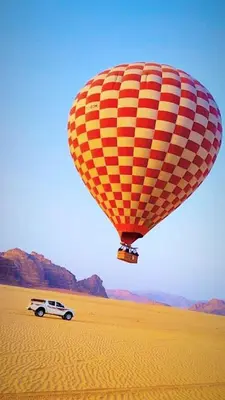 a hot air balloon flying over a car in the desert at وادي رم in Wadi Rum