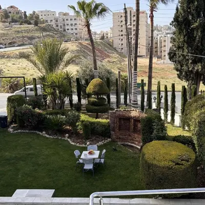 a garden with a table and chairs and palm trees at Al-Farouq Suites in Amman