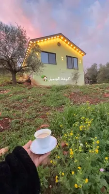 a person holding a cup of coffee in front of a house at Cherry farm in Ajloun