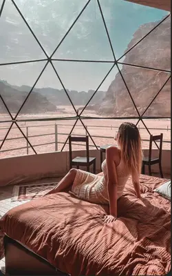 a woman sitting on a bed in front of a window at Rum Magic Bubbles in Wadi Rum