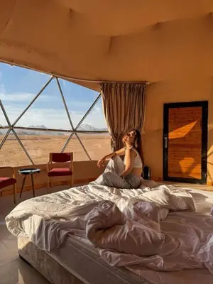 a woman sitting on a bed in front of a window at Rum Magic Bubbles in Wadi Rum