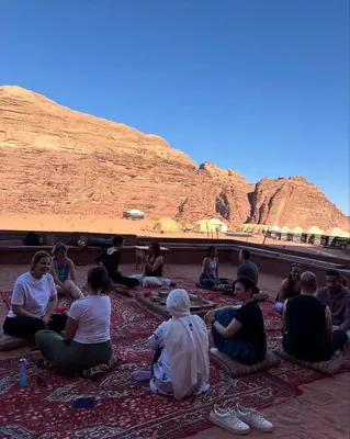 a group of people sitting on the ground in front of a mountain at Thirteen Luxury Camp Valley in Wadi Rum