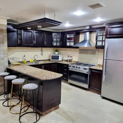 a kitchen with wooden cabinets and a large island with bar stools at Deir Ghbar Suite in Amman