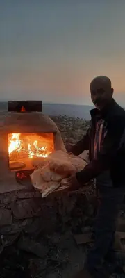 a man is standing next to a pizza oven at اربد ام قيس طريق درب الاردن in Um Qeis