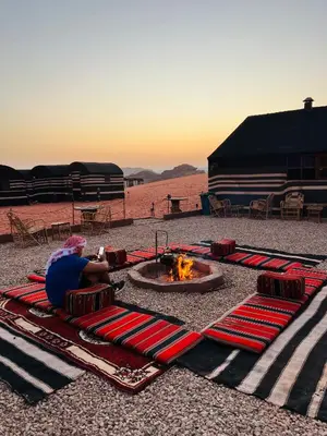 a person sitting on a blanket next to a fire pit at Desert Key Camp in Wadi Rum