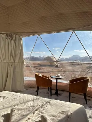 a bed and two chairs in a room with a view at RUM HORIZON BUBBlE LUXURY CAMP in Wadi Rum